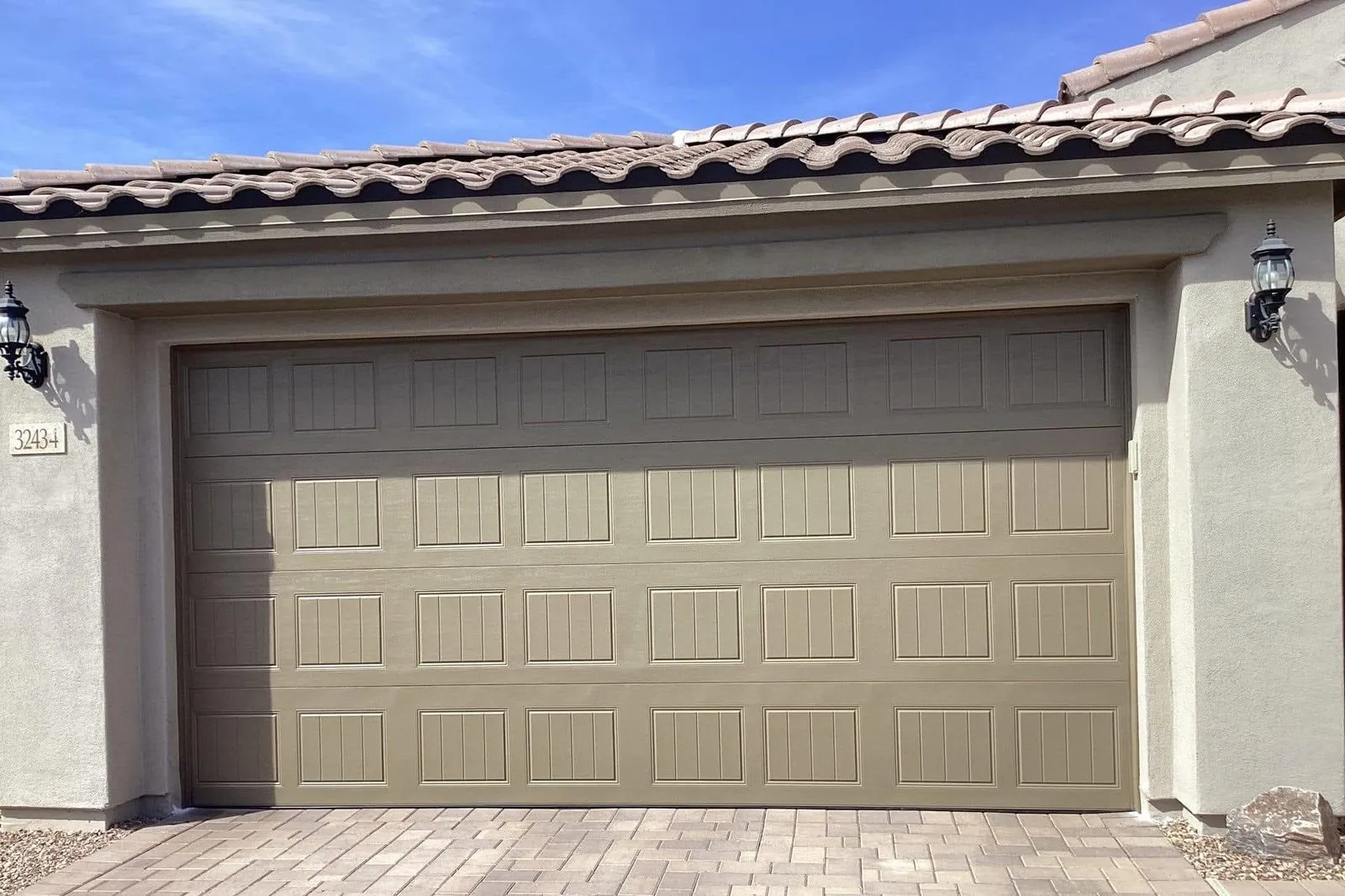 Tan carriage-style garage door on a stucco home with a paver driveway